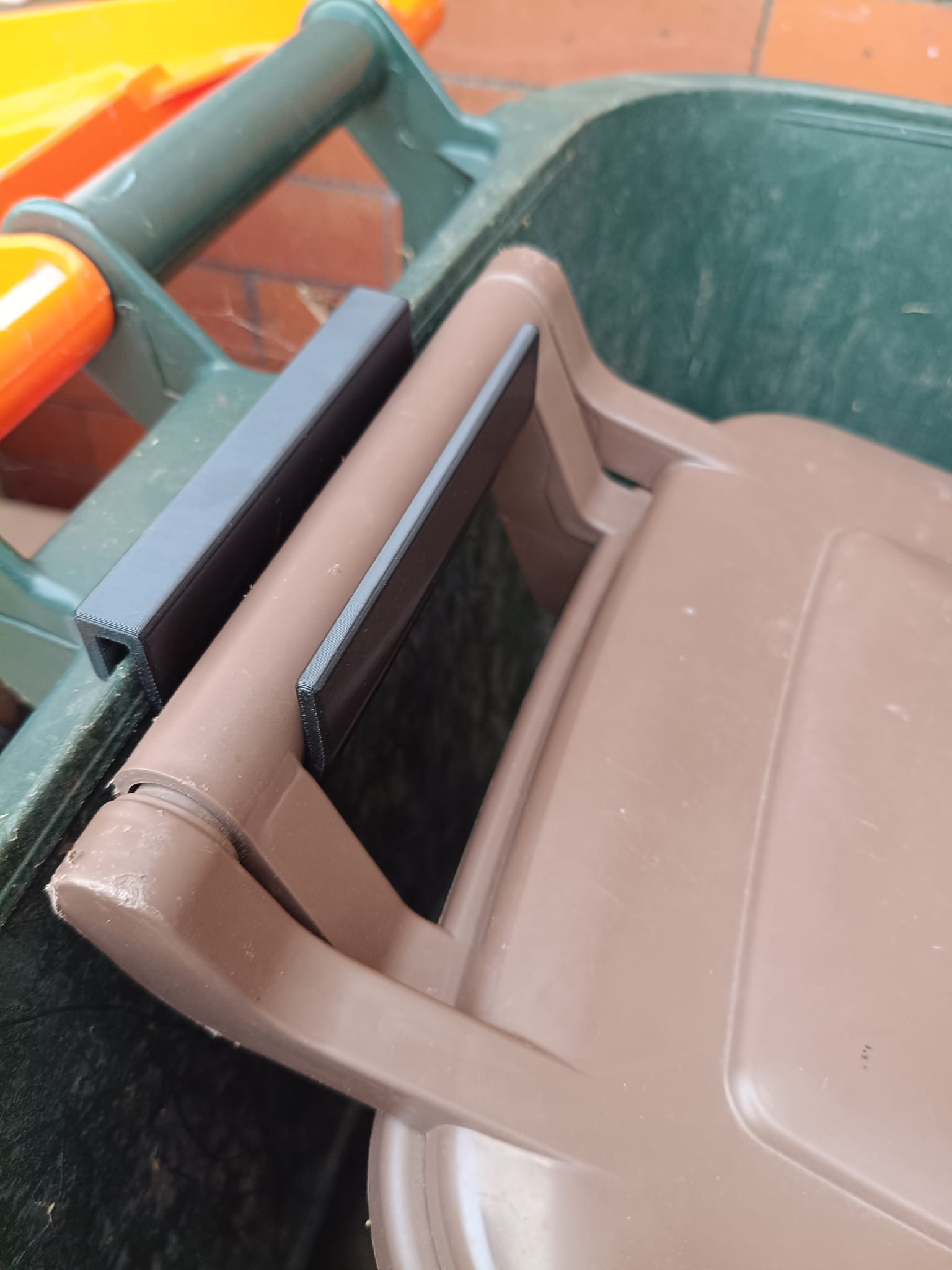 The hook holding a brown food-waste caddy hung inside a green wheelie bin